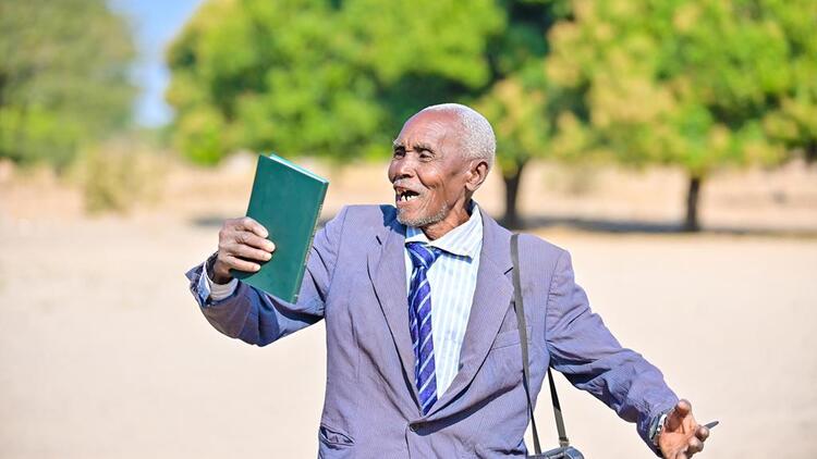 A elderly man celebrating seeing and holding the Kwamashi New testament Bible for the first time